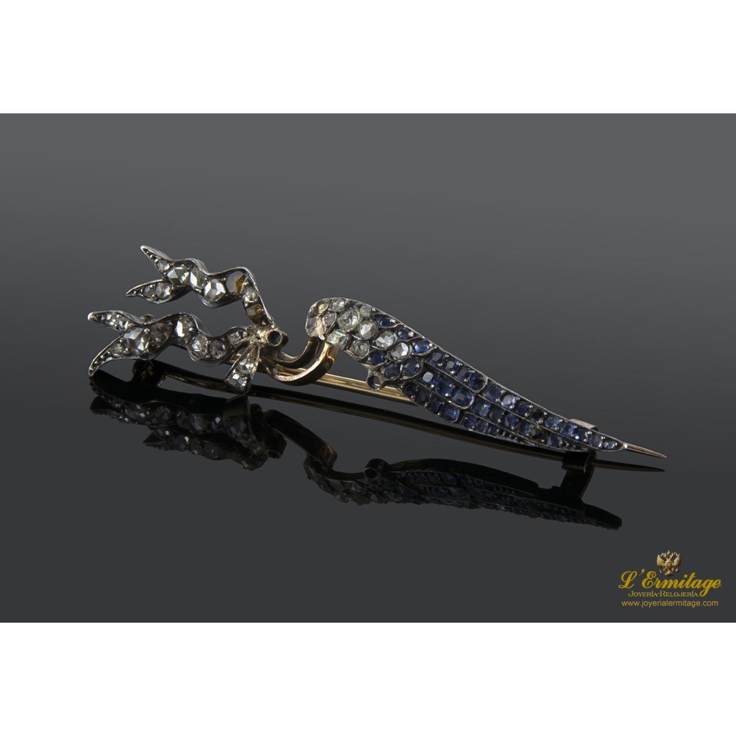 Broche en forma de ala con banderines realizado en oro amarillo y plata. Presenta diamantes y zafiros.